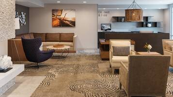 A modern lobby with a sofa, armchairs, a patterned rug, and a reception desk.
