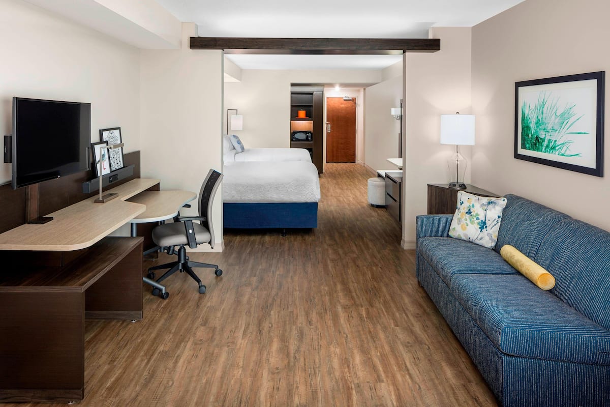 Una habitación de hotel con una cama, un escritorio con computadora, televisor y sofá.