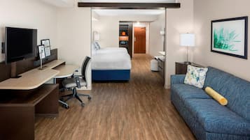 A hotel room with a bed, a desk with a computer, a television, and a sofa.