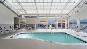 Une piscine intérieure avec des marquages bien visibles, des chaises longues et une vue dégagée grâce à de grandes fenêtres.