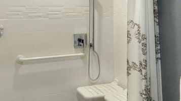 Ein modernes Badezimmer mit weiß gefliesten Wänden, einer Dusche inklusive Handbrause, einer Toilette und einem weißen Waschbecken.