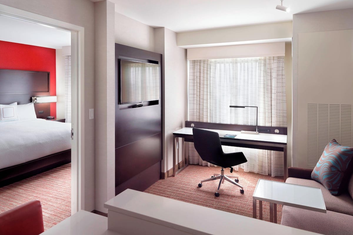 A hotel room with a bed, a desk with a chair, a small table, and a sofa.