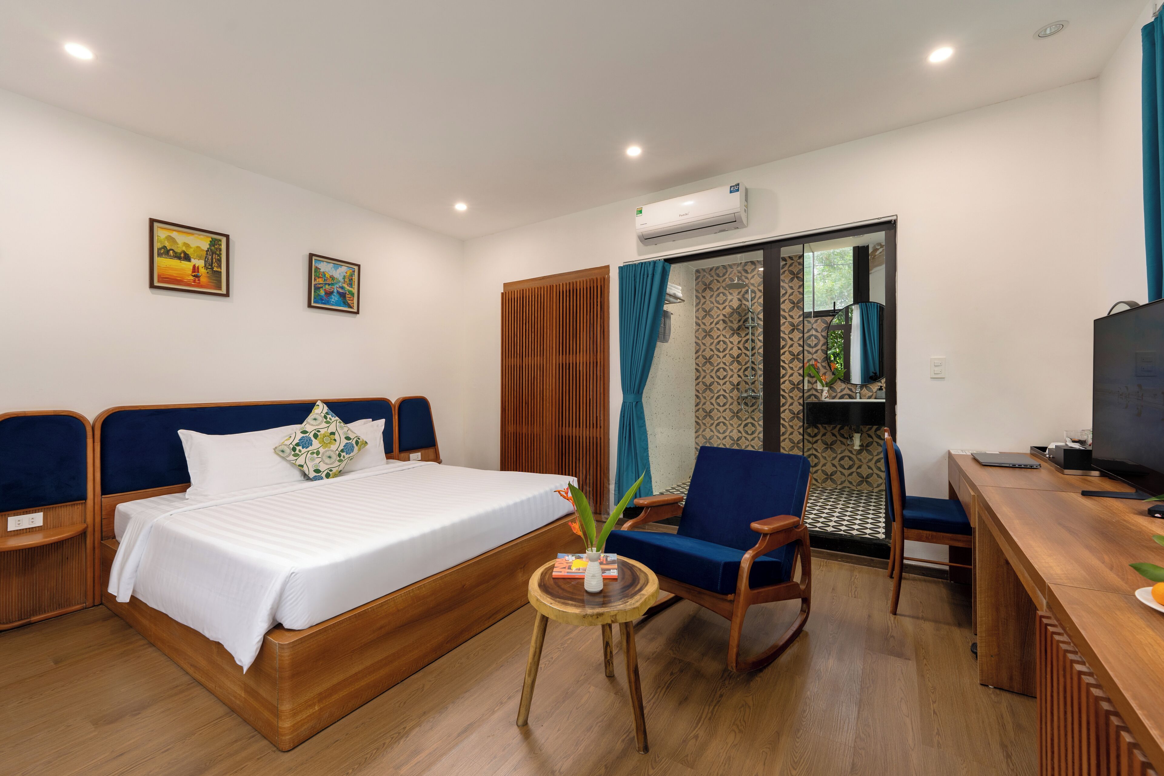 A hotel room with a bed, a desk, a chair, and a small table with a plant.