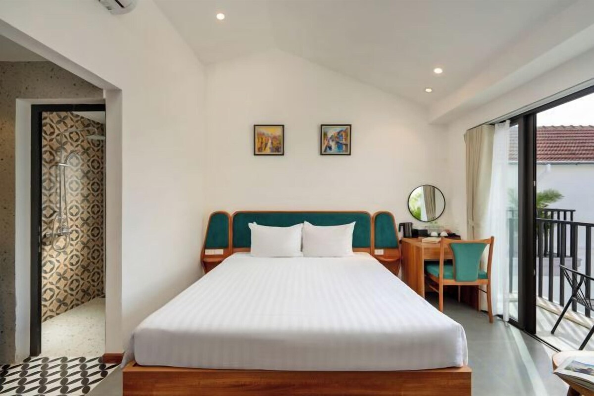 A hotel room with a large bed, a desk, a chair, and a balcony with a view.