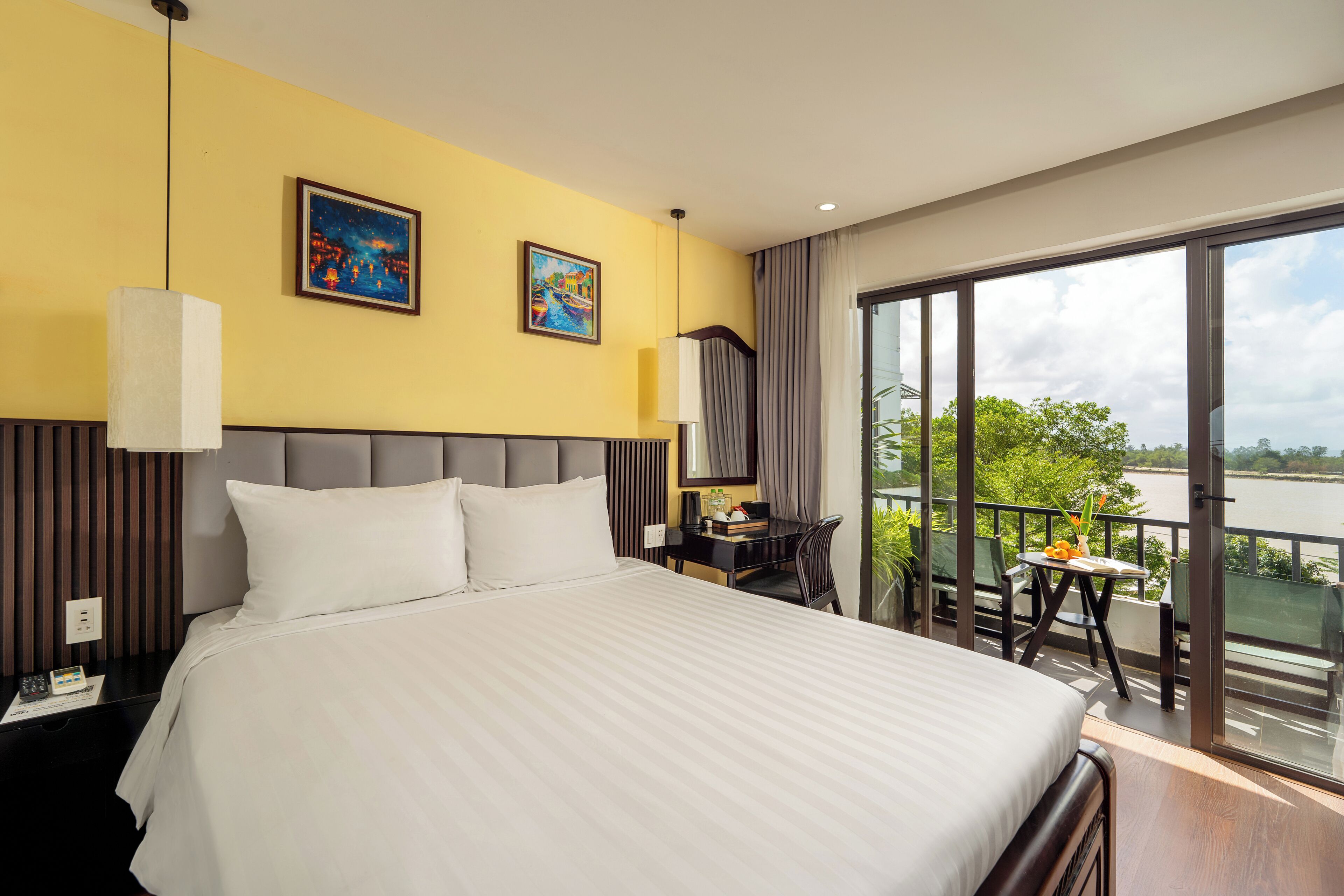 A hotel room with a large bed, a desk, a chair, and a balcony with a view of the water.