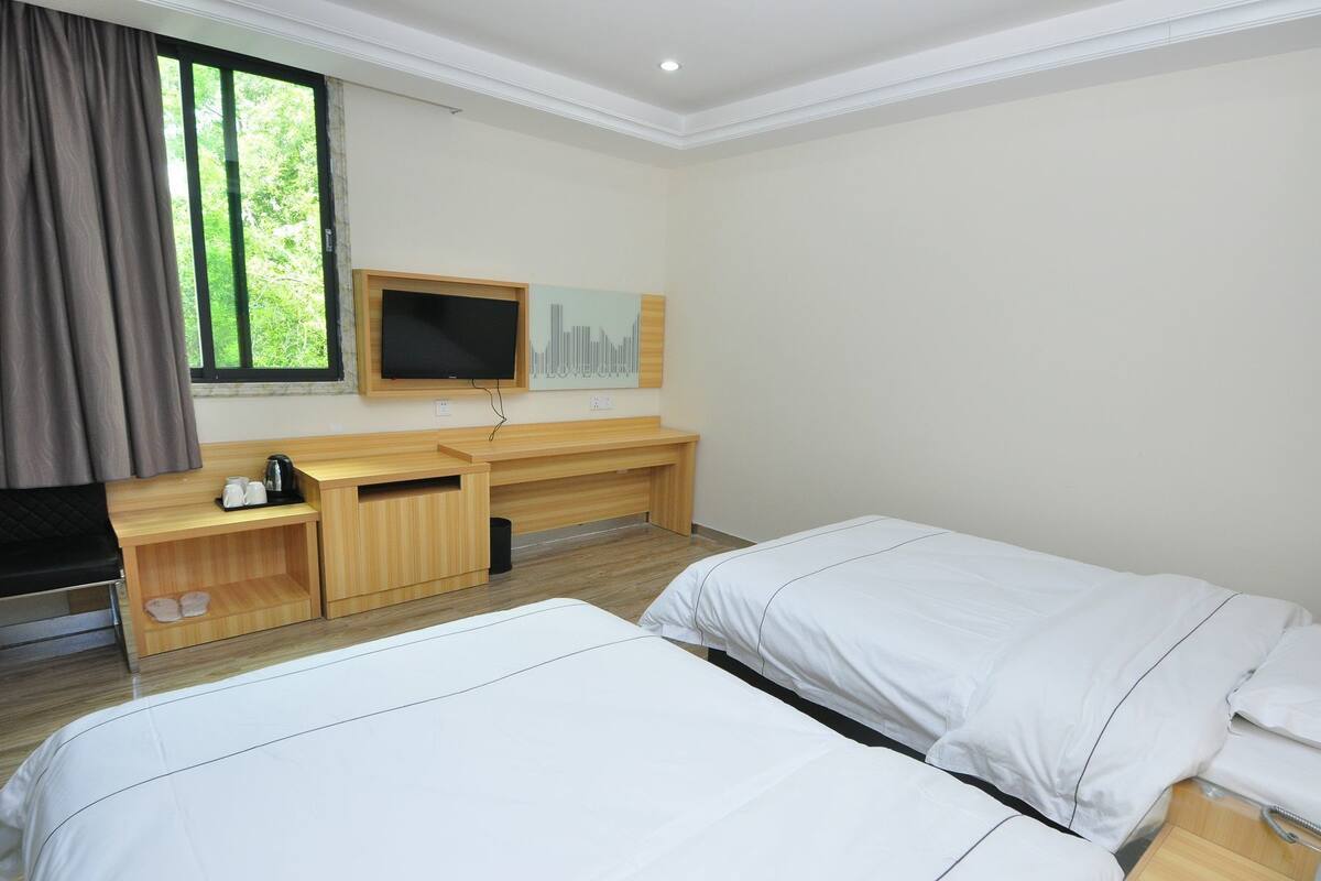 A hotel room with two beds, a desk with a TV, and a window with curtains.