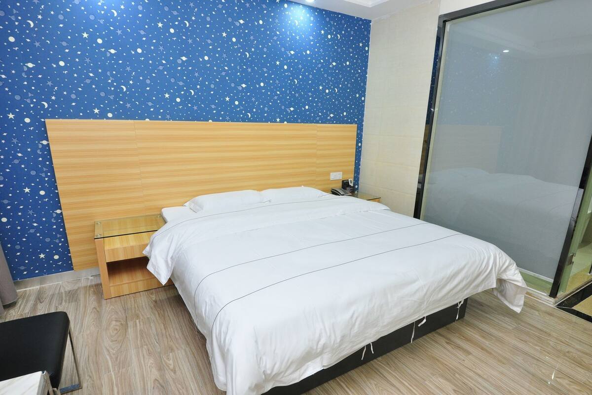 A bedroom with a star-patterned wall, a wooden headboard, a bed with white bedding, a bedside table with a phone, and a sliding glass door.