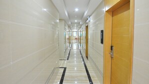 A modern hotel corridor with a marble floor, wooden doors, and a ceiling with recessed lighting. - Jiamei Hotel (Guangzhou)