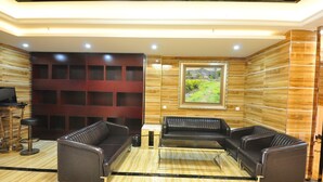 A modern lounge area with leather sofas, a wooden wall with a grid pattern, and a framed landscape painting. - Jiamei Hotel (Guangzhou)