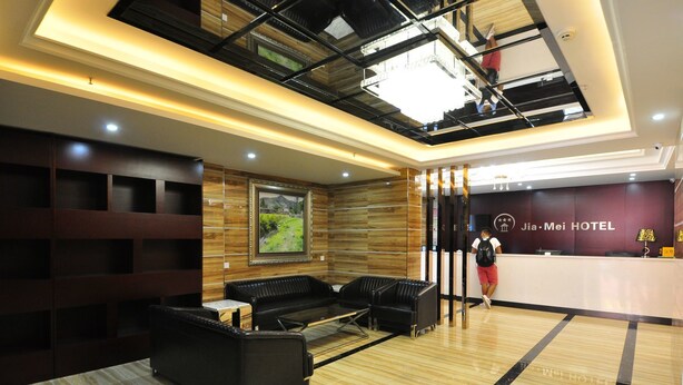 A modern hotel lobby with a reception desk, black leather sofas, a wooden wall with a framed picture, and a high ceiling with exposed beams. - Jiamei Hotel (Guangzhou)