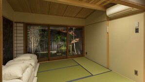 A traditional Japanese room with tatami flooring, a futon bed, sliding doors with a view of a garden, and a ceiling-mounted air conditioner. - Shimabara Kaiden (Kyoto)