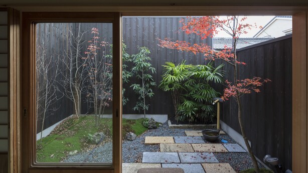 A view through a sliding door of a garden with a wooden fence, various plants, and a stone pathway. - Shimabara Kaiden (Kyoto)