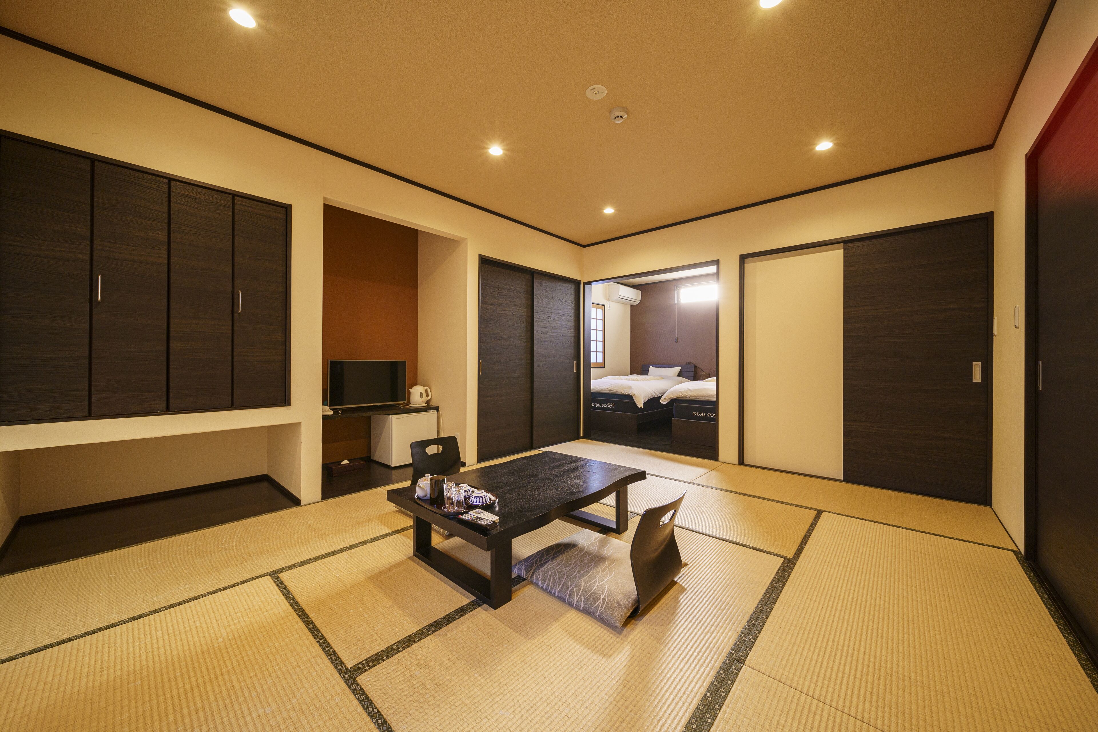 A modern hotel room with a tatami mat floor, a dark wooden table, and a bed with a white headboard.