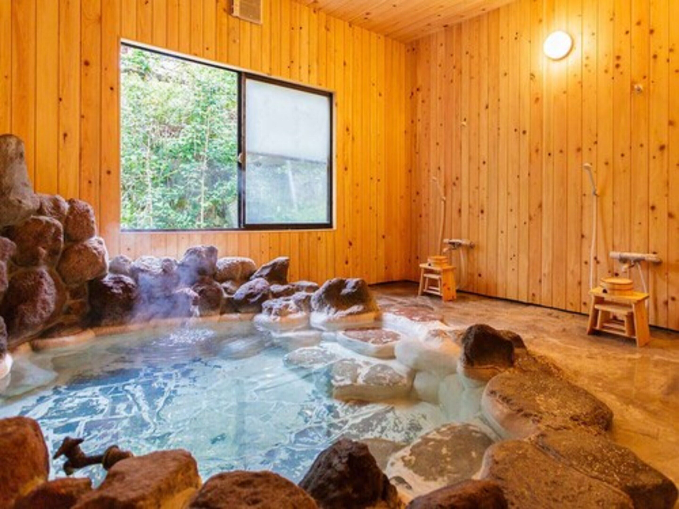 A hot spring bath with rocks, wooden walls, and a window.