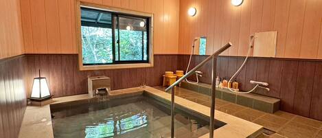 Habitación con paneles de madera, un jacuzzi con paredes de vidrio, una ventana con vistas y un taburete pequeño.