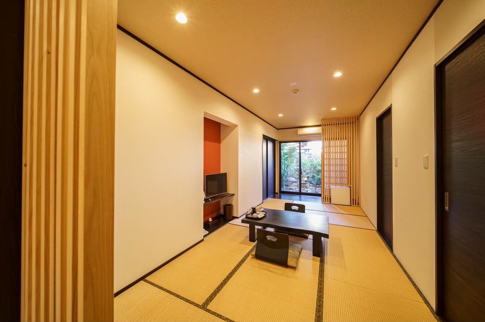 Un pasillo con esteras de tatami, una puerta corredera, un televisor y una pequeña mesa con sillas.