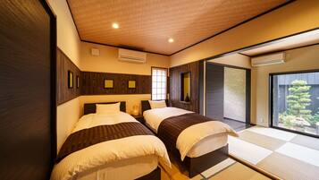 Habitación de hotel con dos camas, paneles de madera, un ventanal y vista a un jardín.