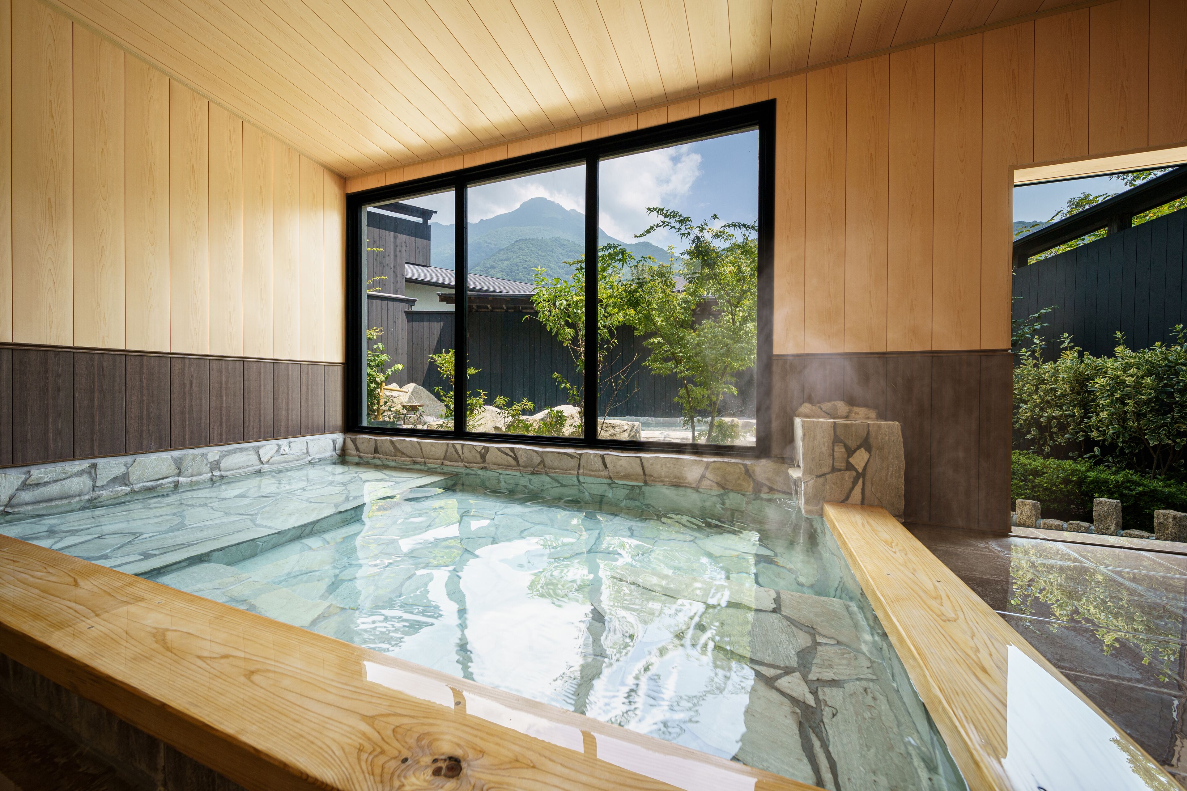 A hot spring bath with a wooden interior, large windows, and a view of mountains.