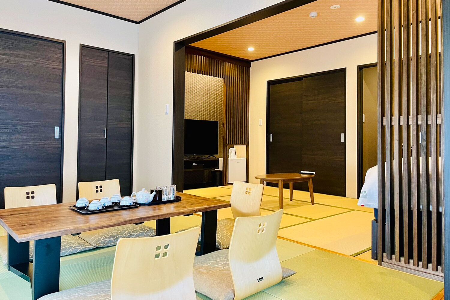 Habitación de hotel moderna con una mesa de comedor de madera, sillas cómodas, televisor y una puerta corredera japonesa tradicional.