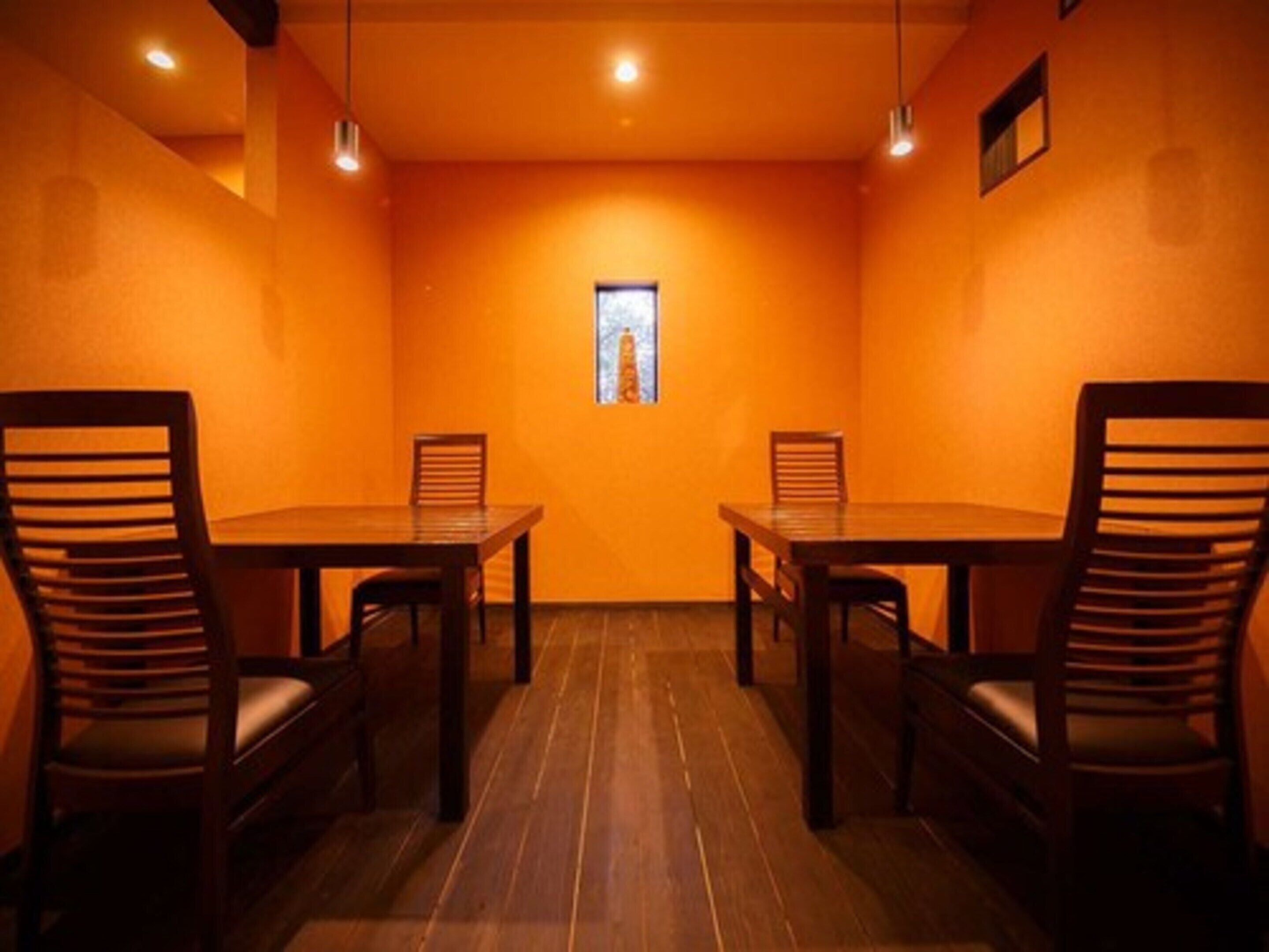 A conference room with two wooden tables and chairs, orange walls, and a small window.