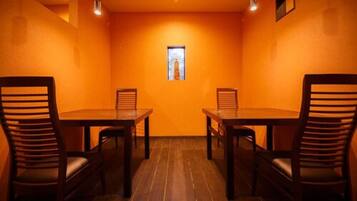 A conference room with two wooden tables and chairs, orange walls, and a small window.
