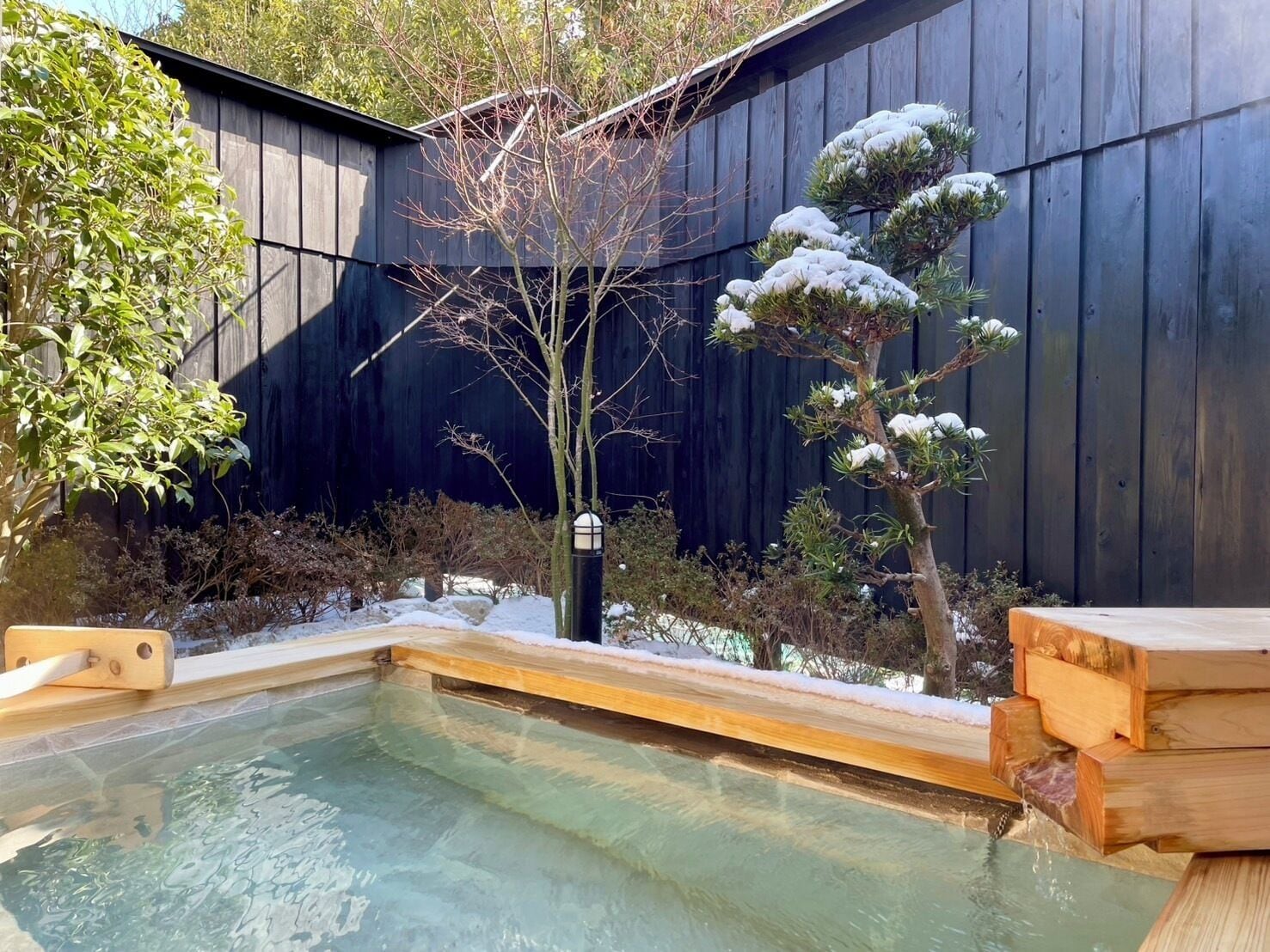 A hot spring area with a wooden deck, a small pool, and a wooden fence in the background.