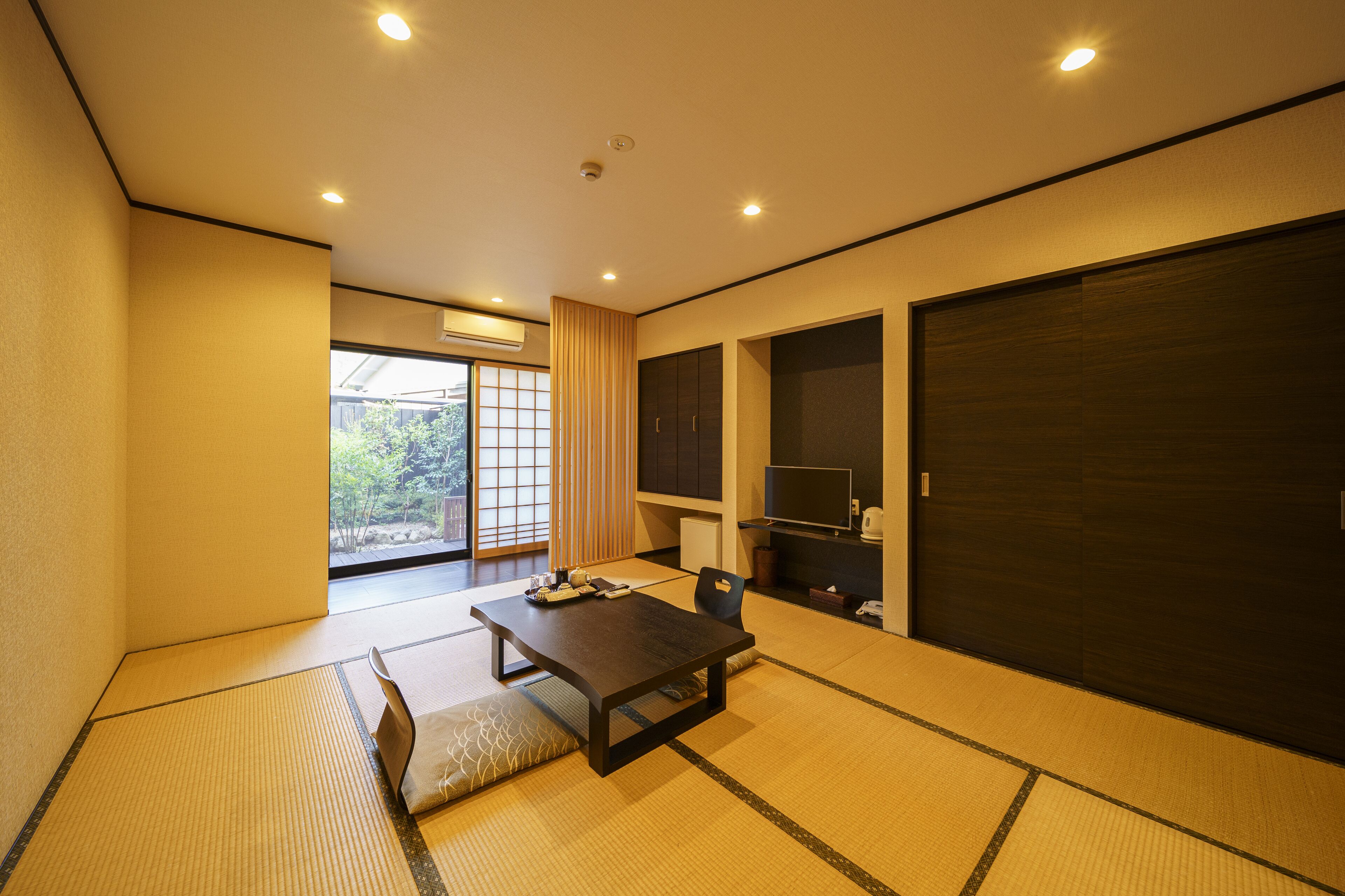 A traditional Japanese room with tatami flooring, a low table, a chair, sliding doors, and a TV.