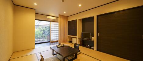 A traditional Japanese room with tatami flooring, a low table, a chair, sliding doors, and a TV.