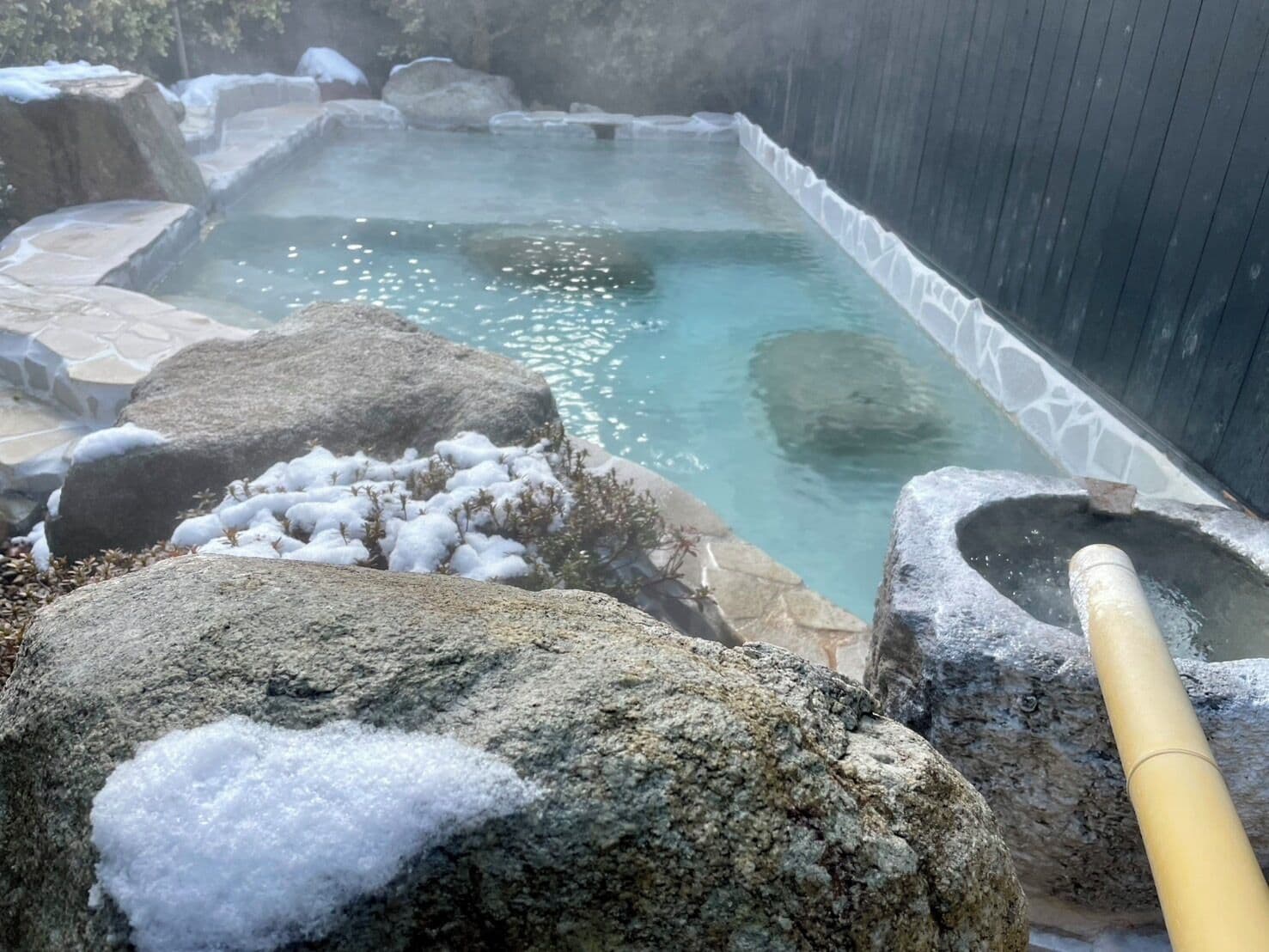 A hot spring area with a stone pool, rocks, and a wooden structure.