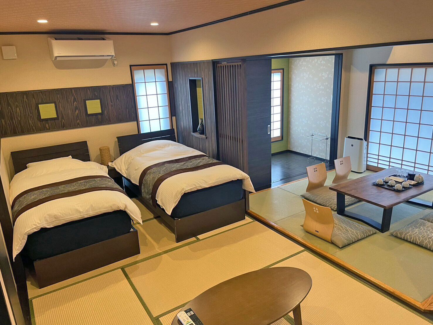A hotel room with two beds, a small table with snacks, a chair, and a view of the outside.