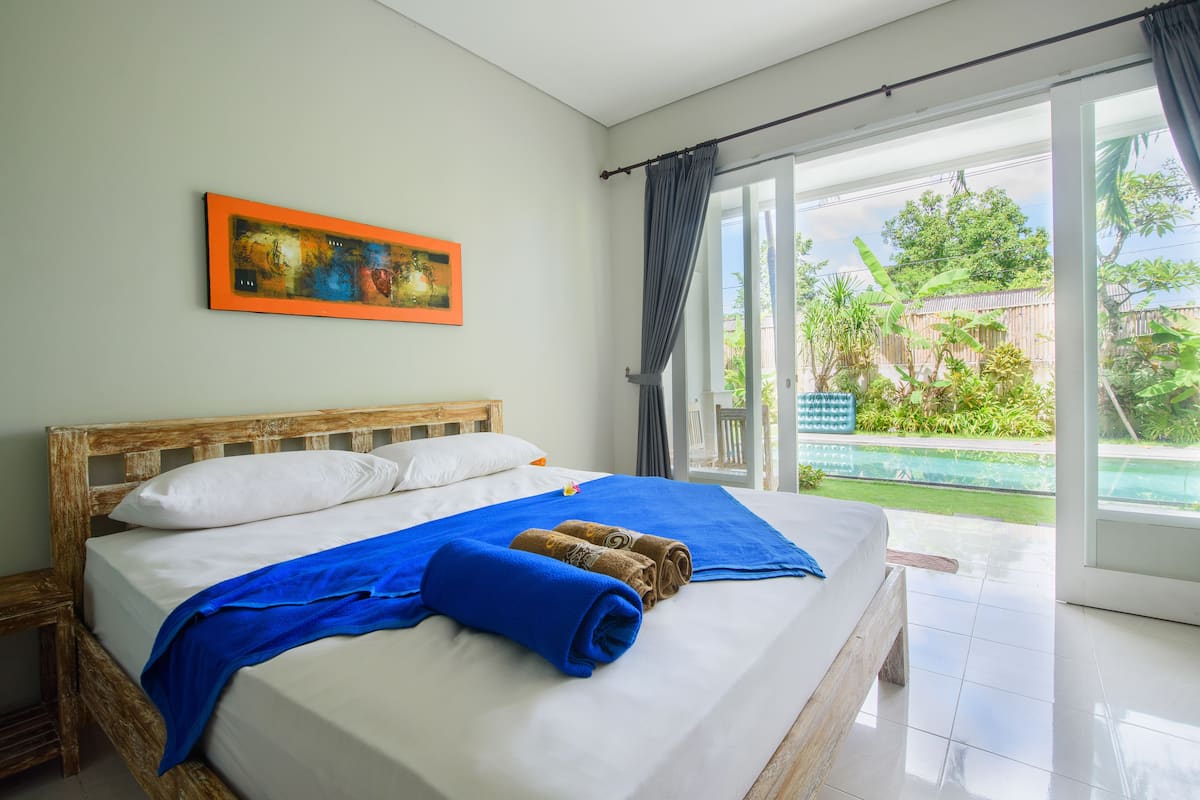 Une chambre d’hôtel avec un lit en bois, une couverture bleue et un tableau accroché au mur.