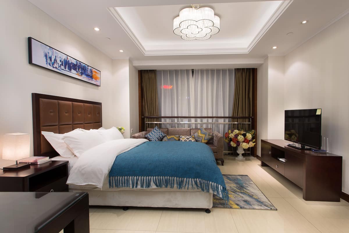 Ein modernes Hotelzimmer mit einem großen Bett, einem Fernseher, einem Schreibtisch und einer Deckenleuchte.