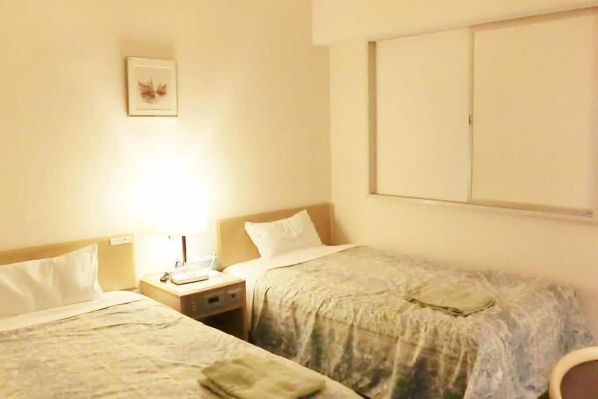 A hotel room with two single beds, a nightstand with a lamp, a chair, and a wardrobe.