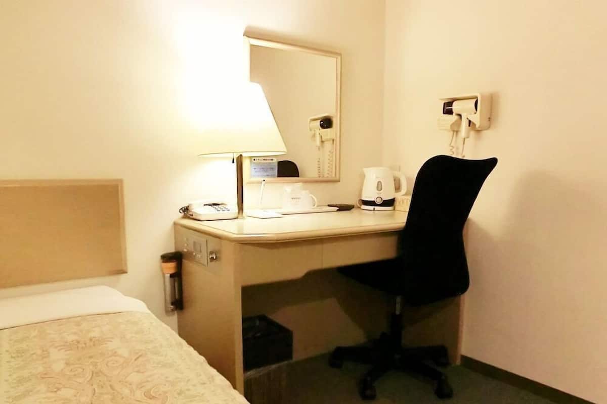 A hotel room with a bed, a desk with a lamp, a telephone, a coffee maker, and a chair.