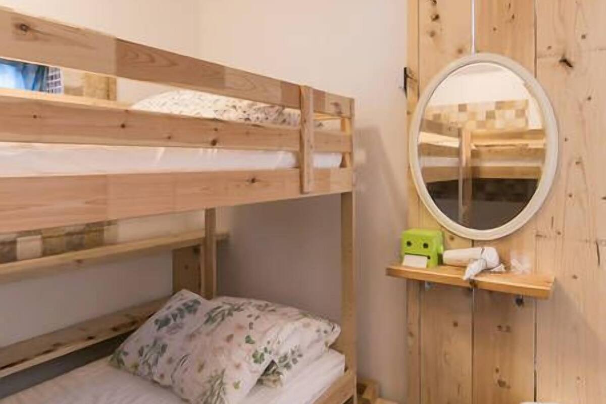 Une chambre avec un lit superposé, une tête de lit en bois, un miroir rond et une petite étagère contenant des articles de toilette.