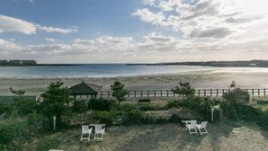 Blick auf einen Strand mit einer Laube, zwei Liegestühlen und einem Holzzaun.