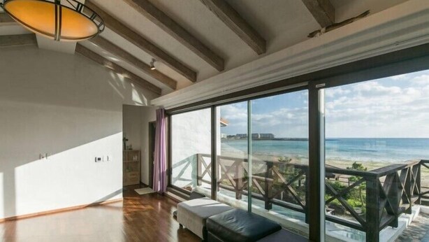 Ein Zimmer mit großem Fenster und Meerblick, Holzboden und einer Bank am Fenster.
