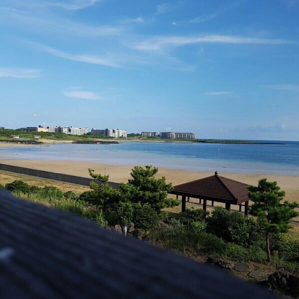 Vista de una playa con un quiosco de madera, una orilla arenosa y edificios al fondo.