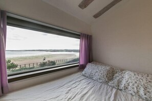 Een slaapkamer met een bed, een raam met uitzicht op een strand en een houten balk in het plafond.