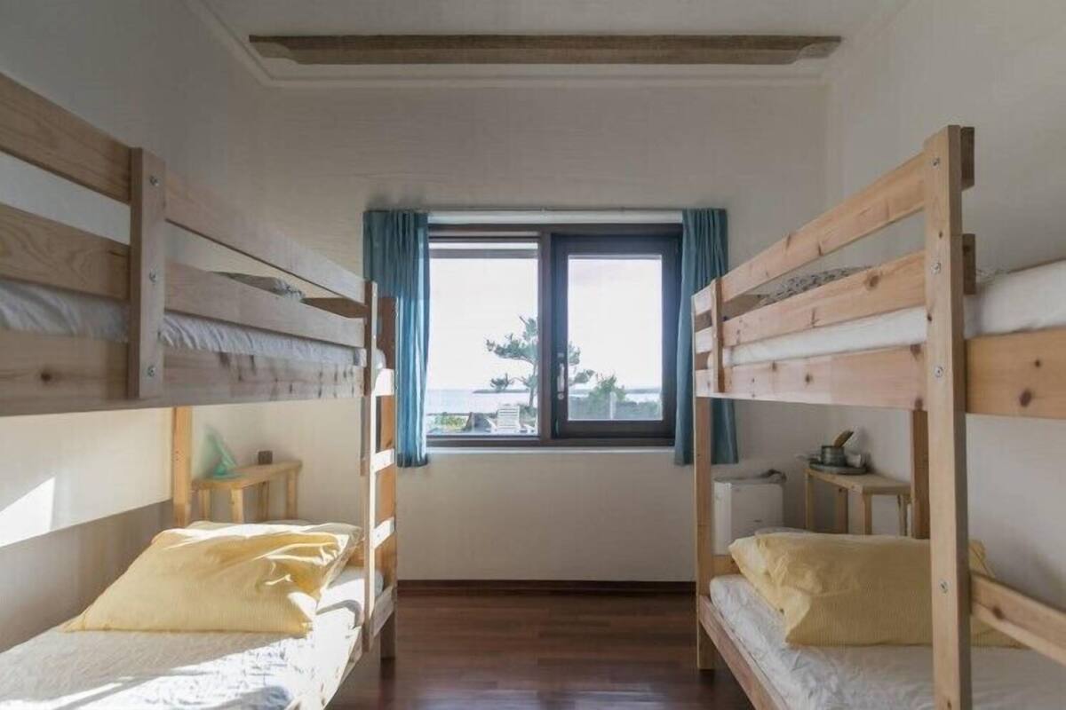 Une chambre avec deux lits superposés, une fenêtre avec des rideaux, une petite table et un radiateur.