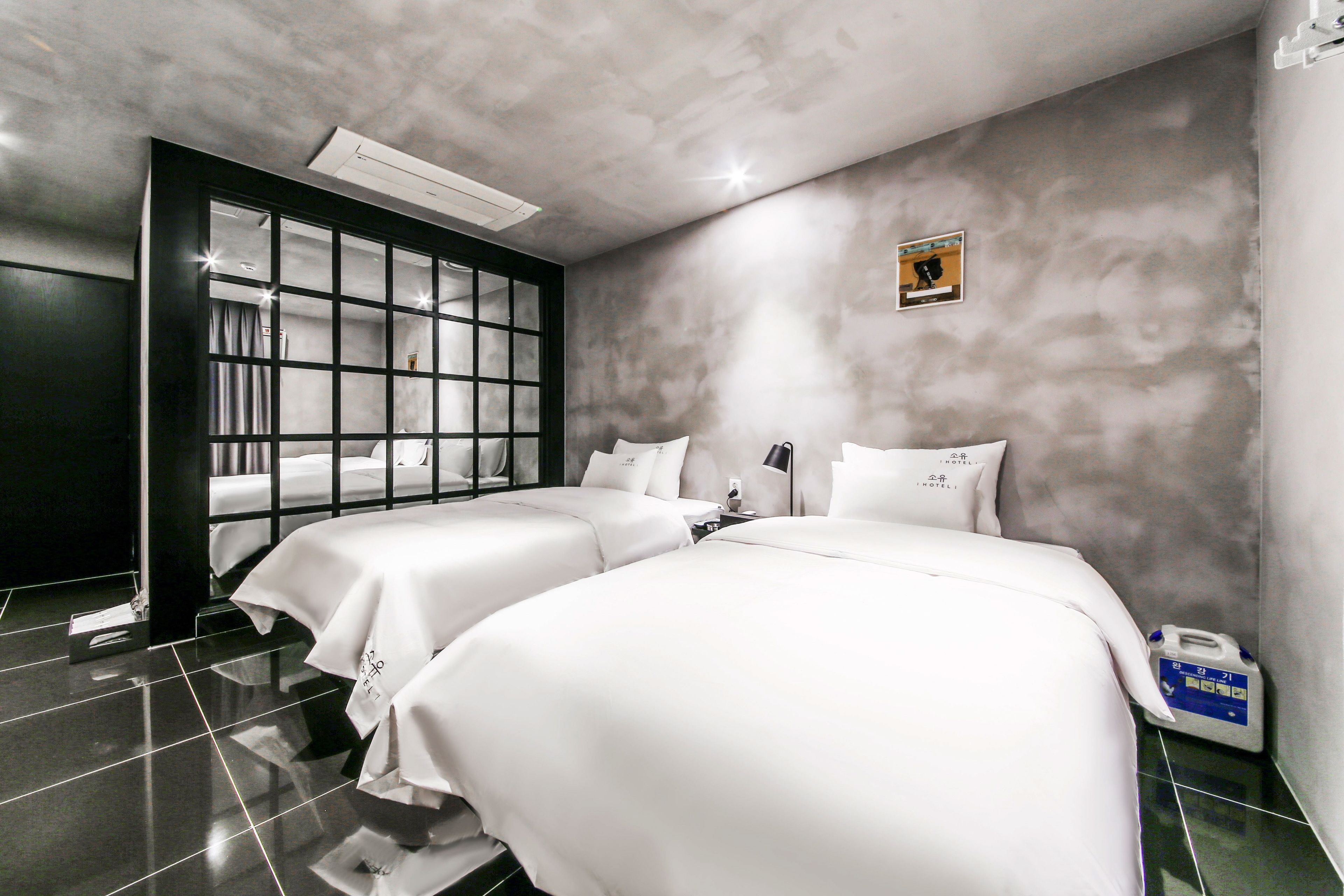 Habitación de hotel con dos camas, un ventanal grande y un aire acondicionado instalado en la pared.