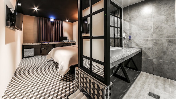 A modern hotel room with a checkered floor, a bed with a white cover, a desk with a computer, and a bathroom with a granite countertop and tiled walls. - SOYU Hotel (Busan)