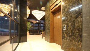 A modern lobby with a marble floor, a wooden elevator, and a large chandelier. - SOYU Hotel (Busan)