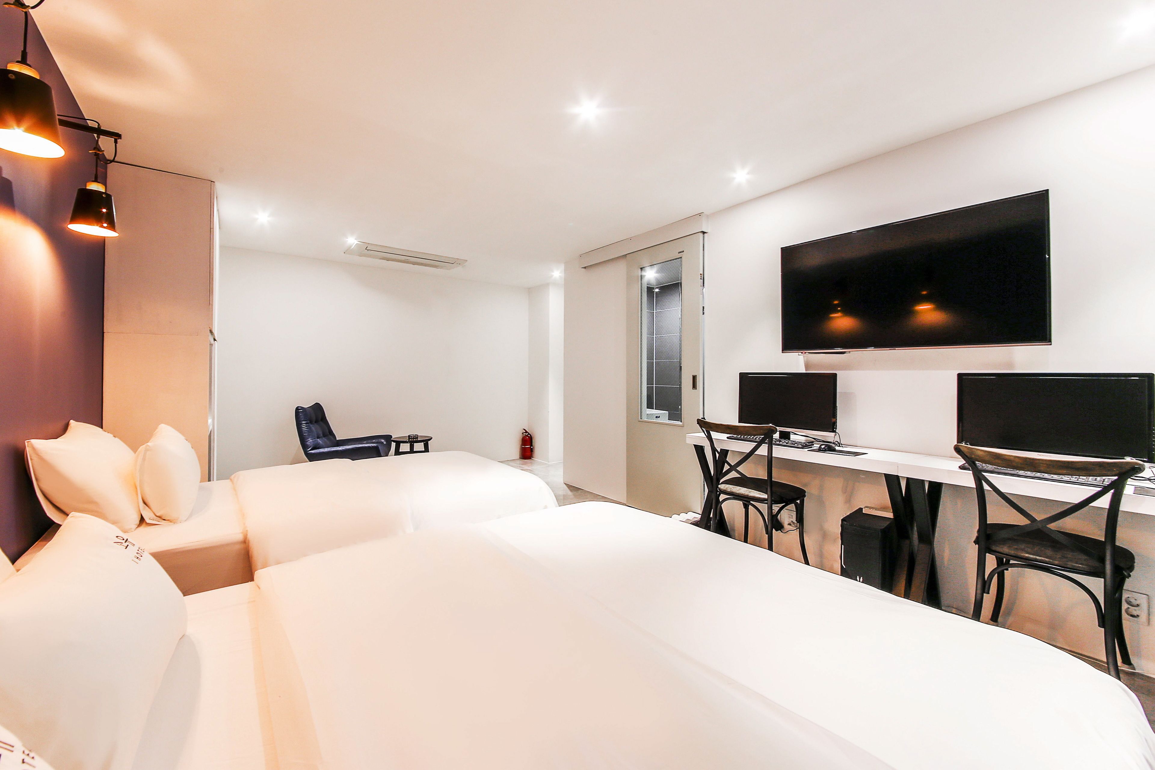 A modern hotel room with two beds, a desk with two monitors, and a flat-screen TV.