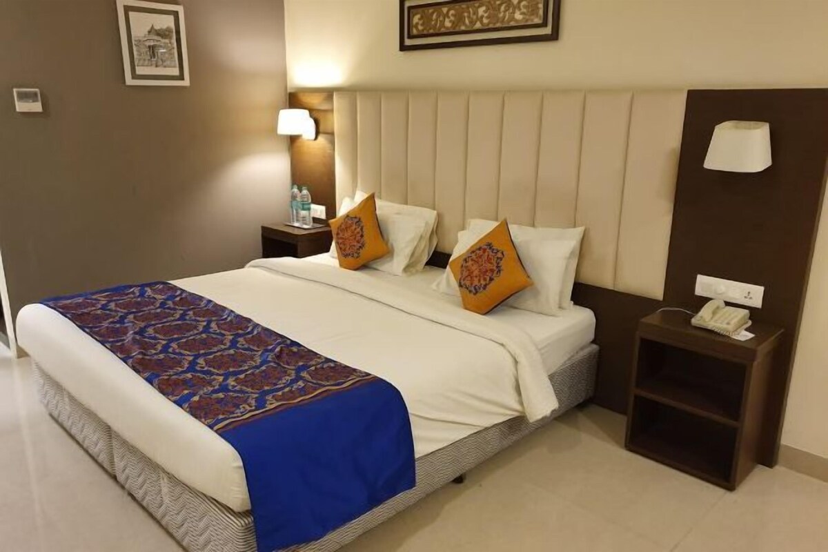 Habitación de hotel con una cama grande, dos almohadas, una mesita de noche con lámpara y teléfono.