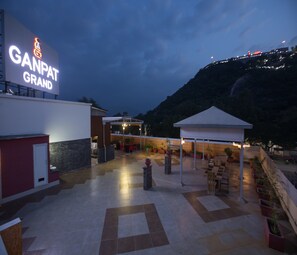 A hotel courtyard with outdoor seating, a covered area, and a mountain backdrop. - Hotel Ganpat Grand, Palani (Palani)