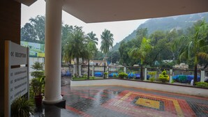 Uma área de recepção com piso molhado, um balcão de recepção e um aviso listando comodidades como o Restaurante AAHARAM e o Salão de Festas Sri Valli.