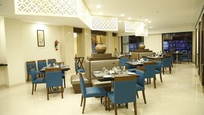 Um restaurante com cadeiras e mesas azuis, um extintor de incêndio e um vaso grande em um pedestal.