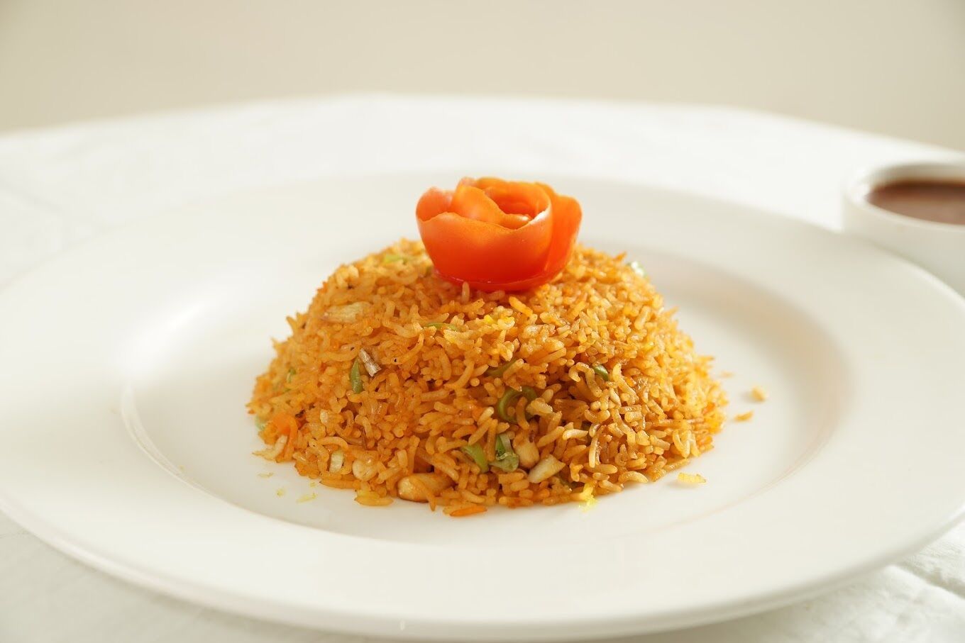 Un plato blanco con una porción de arroz anaranjado coronada con una flor naranja decorativa.