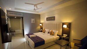 A hotel room with a bed, bedside tables, a desk, a chair, a ceiling fan, and a wall-mounted lamp. - Hotel Ganpat Grand, Palani (Palani)
